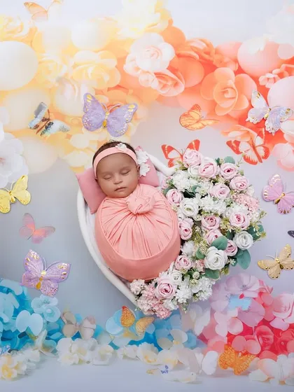 A newborn girl sleeps in a heart-shaped bowl, surrounded by a rainbow of flowers and butterflies. A wide shot of this popular theme.
