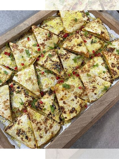 A tray of our savory quesadillas, cut into triangles for easy sharing. Sprinkled with sev and pomegranate, they have a delightful Indian twist.