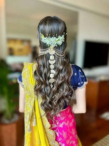 Mastering soft, romantic styles is key for any hairstylist. This look features beautiful, bouncy curls complemented by fresh baby's breath and a statement gold hair accessory, perfect for a mehendi or sangeet.