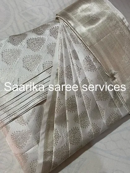 An elegant white saree with silver motifs, professionally folded by Saarika Saree Services.