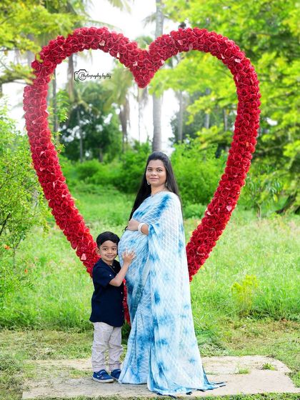 A growing family. The older sibling stands proudly next to his expecting mother in front of our red floral heart prop.