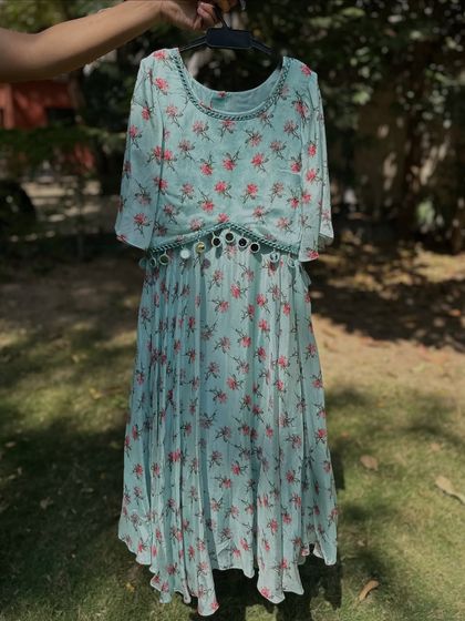 This floral dress in a soft mint color is perfect for summer parties. It features a pleated skirt and a mirror-work belt, adding a touch of festive sparkle to a comfortable design.
