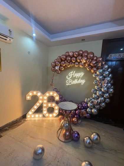 This is a duplicate of ID 37, 80, 136, 139, 158, 203, 247. A stylish half-arch balloon ring for a 26th birthday. This home decoration uses chrome rose gold and silver balloons, a neon sign, and marquee numbers.
