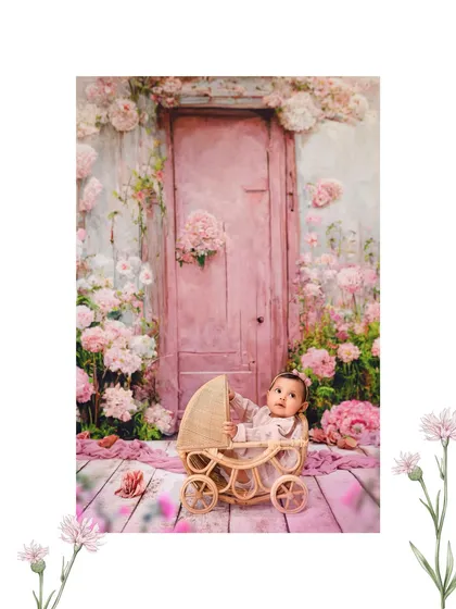 A baby girl sits in a wicker pram against a dreamy pink floral backdrop, part of a magical sibling photoshoot.