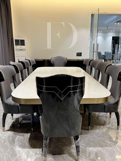 A full view of the 10-seater dining set, highlighting the unique V-shaped design on the back of the chairs. The combination of dark wood, grey upholstery, and gold accents is the epitome of modern luxury.