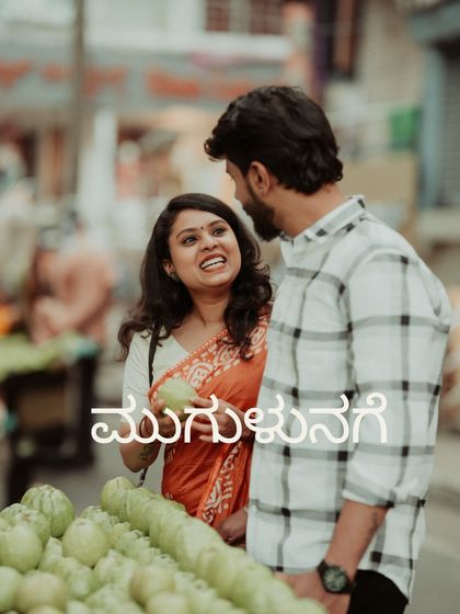 A candid moment of joy and laughter while shopping for fruit at a local market. The Kannada text "Mugulunage" means "smile," perfectly capturing the spirit of this shot.