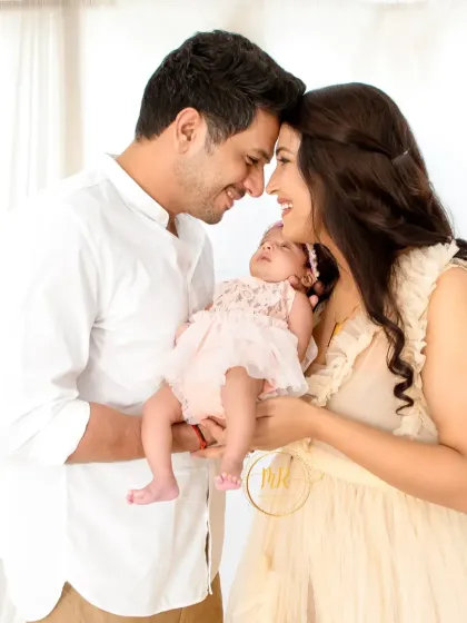 New parents hold their sleeping baby girl, their heads touching in a moment of quiet adoration.