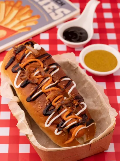 A delicious hot dog loaded with sauces, shot for Who Let The Dogs Out. The bright, checkered background gives it a fun, American diner feel.