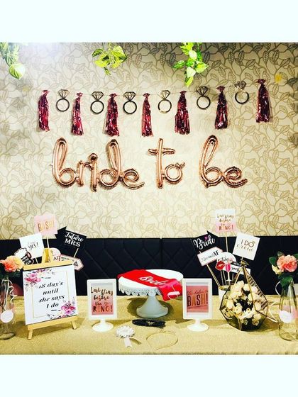 This bachelorette party setup features a 'Bride to be' balloon banner paired with a fun ring and bottle garland. The table is filled with props and signs to get the party started.