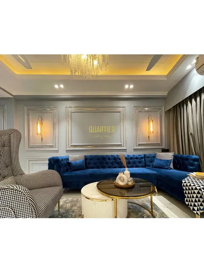 Another angle of the European-inspired living room at Elite Golf Greens. The combination of the tufted blue sofa, houndstooth armchair, and elegant wall mouldings creates a sophisticated and timeless look.