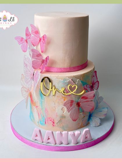 A dreamy butterfly cake for Aanya's first birthday. This two-tiered design features a pastel watercolor effect and is covered in delicate pink butterflies.