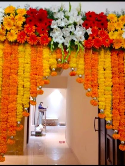 A main door decoration for a housewarming using marigold and other colorful flowers. The hanging garlands create a beautiful curtain effect.