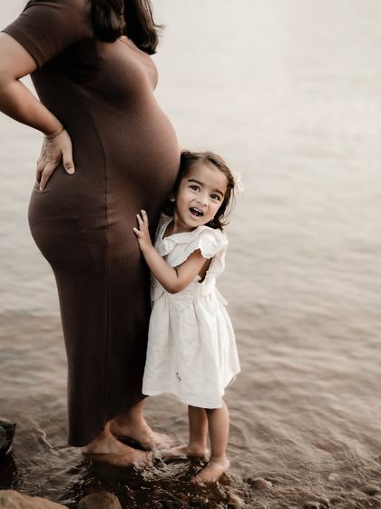 A joyful and candid moment. The little girl hugs her mom's baby bump with a huge smile, absolutely thrilled about becoming a big sister.