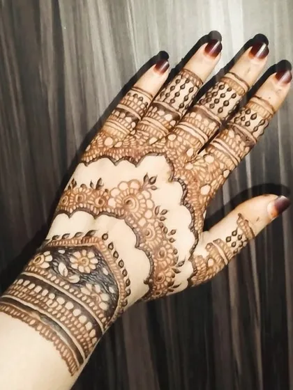 A detailed look at a scalloped cuff design on the wrist and delicate patterns on the fingers. The darkened fingertips are a traditional element that my henna achieves beautifully.