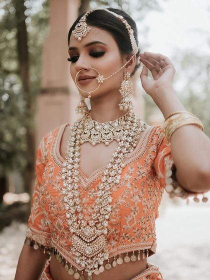 A close-up on the stunning, heavy pearl and stone jewellery set against the peach lehenga, showing how accessories can elevate the entire look.