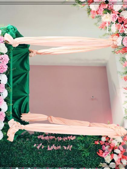 This shot shows the details of the cradle and the floral arch. The cradle is draped in green fabric and adorned with flowers, suspended by soft pink sashes.