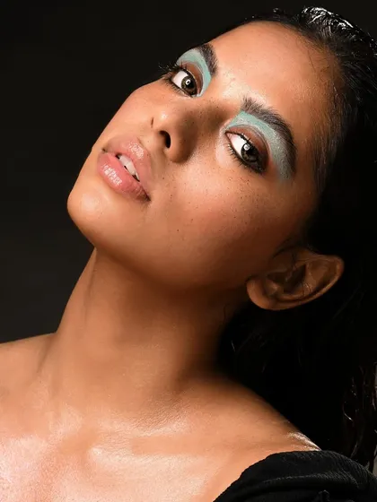 A raw, edgy editorial look. The focus is on the block of turquoise eyeshadow and the dewy, almost wet, skin finish, which are popular trends in fashion photography.