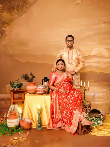 A lovely couple's portrait from a Bengali-themed maternity shoot. The setting includes traditional elements like earthen pots and a painted backdrop, perfectly complementing their ethnic attire.