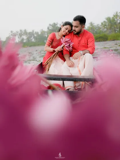 A close-up view of the couple in the boat, framed by vibrant pink water lilies. This perspective creates a very intimate and dreamy feel.