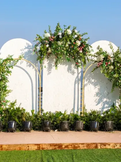 A clean, modern backdrop perfect for a daytime event by the sea. The white arched panels are accented with gold trim and lush floral arrangements, creating a look that is both fresh and sophisticated.