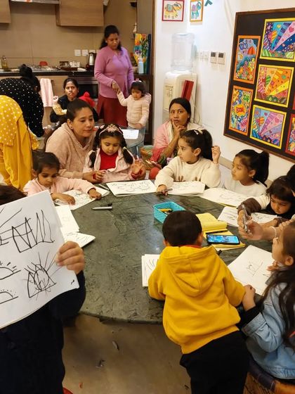 A teacher demonstrates a drawing technique to an eager group of toddlers. We use simple, recognizable shapes to build their drawing confidence.