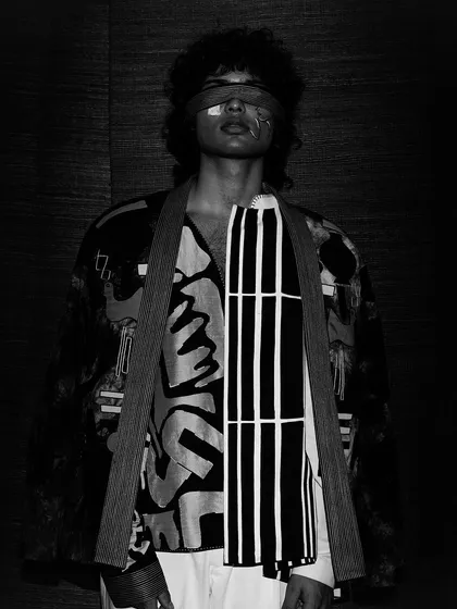 Another dramatic black and white shot, where the model's blindfolded face is partially obscured by shadow. The bold lines and patterns of the clothing stand out, creating a visually complex image.