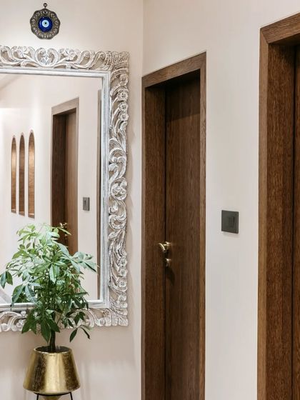 An ornate, carved white mirror adds a touch of vintage glamour to this hallway. Paired with a simple plant in a gold pot, it creates an elegant focal point while also making the space feel larger and brighter.