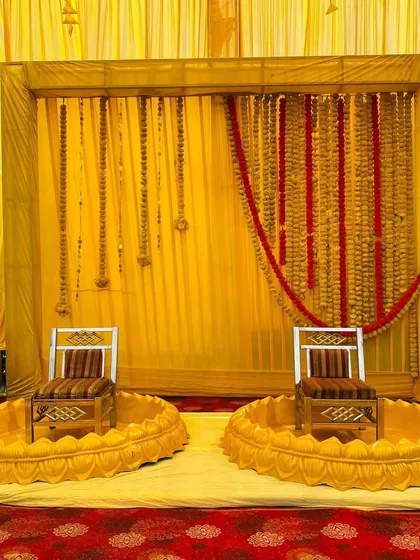 A traditional Haldi seating arrangement with low, lotus-shaped seats and a backdrop of yellow drapes and marigold garlands.