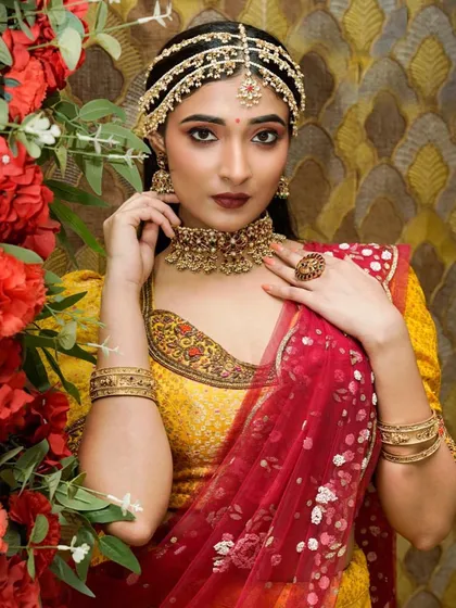 A model in a yellow and red lehenga, wearing a gold-finish choker and a delicate matha patti for a North Indian inspired look.