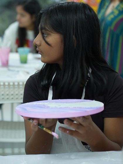 Another shot of a student during a workshop, holding up her circular canvas. We offer a wide range of experiences, from canvas painting to pottery, so there's always something new to try.