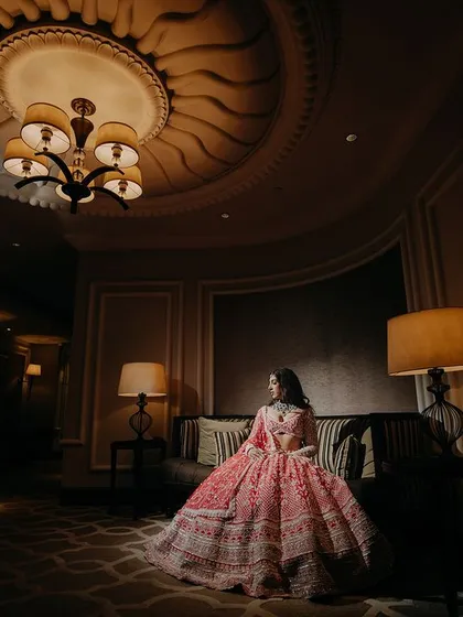 A wide, atmospheric shot of the bride in a luxurious room. The warm, ambient lighting and classic decor create a moody and sophisticated setting for this elegant bridal portrait.
