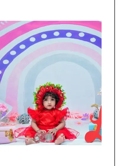 A sweet, simple portrait of the baby girl in her red dress and bonnet. The focus is on her curious expression, with the soft rainbow background adding a touch of color.