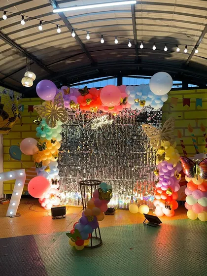 This butterfly-themed party features a rainbow of balloons against a silver shimmer wall, creating a vibrant and sparkling effect.