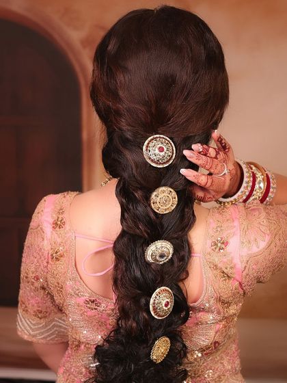 A close-up of a stunning bridal braid. This hairstyle is decorated with large, traditional, kundan-style hair accessories, adding a regal and unique touch to the overall look.