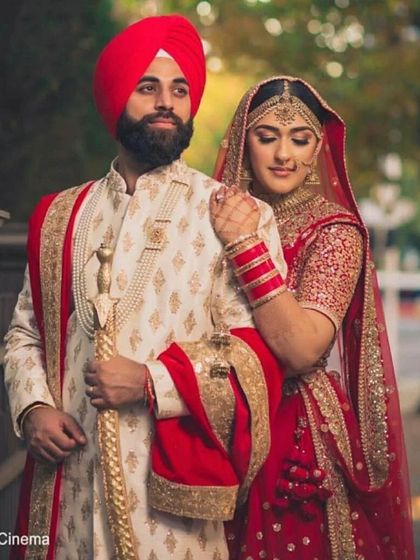 A powerful portrait of a Sikh couple. The groom is wearing a cream and red sherwani with a matching red turban, holding a ceremonial sword.