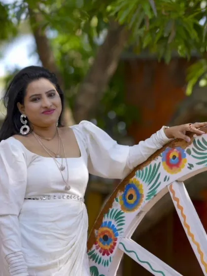 A beautiful solo portrait of a woman in a stylish white saree, posing with a colorful painted wheel prop. Perfect for a birthday or personal branding shoot.