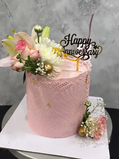 A blushing pink anniversary cake. This tall design is adorned with a beautiful arrangement of fresh lilies and roses, delicate piping, and flecks of gold leaf for a touch of magic.