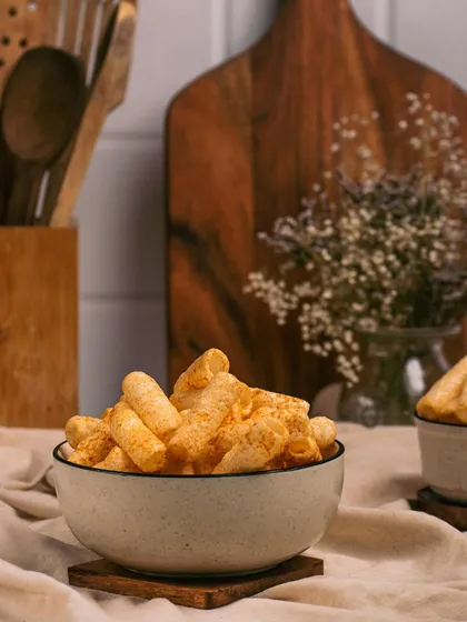 A bowl of savory snacks styled in a kitchen setting with wooden props and a rustic cloth. This lifestyle approach makes the product feel like a part of a cozy, everyday moment.