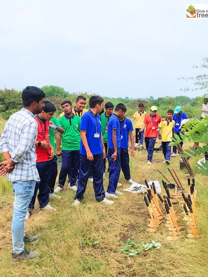 An instructor explains the planting process to a group of students, showing them the tools and saplings before they begin.