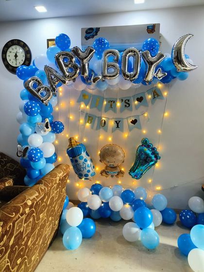 A lively 'It's a Boy' decoration for a home celebration. The setup includes a blue and white balloon arch, fairy lights, and multiple themed foil balloons.