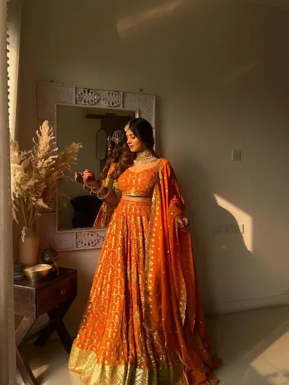 A full view of the orange bandhani lehenga. The flowing fabric and traditional print make it a classic choice for pujas, mehndi functions, or family gatherings.