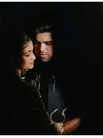An intimate, artistic portrait using the chiaroscuro technique. The dramatic play of light and shadow creates a moody and romantic feel, perfect for a Sangeet night couple shoot.