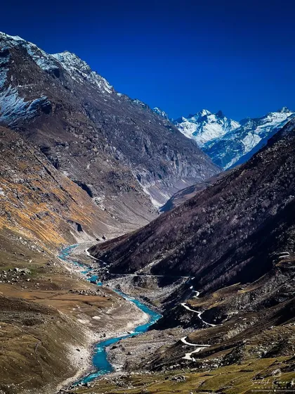 The vast, high-altitude desert of Spiti Valley unfolds under a brilliant blue sky. This landscape shot captures the winding river and snow-capped Himalayan peaks, reflecting the scale and raw beauty of my expeditions into remote India.