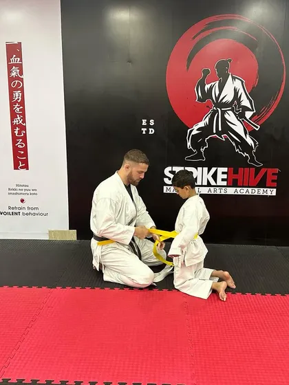 A coach ties a new yellow belt for a young student. This moment represents a significant step forward, earned through dedication and practice.