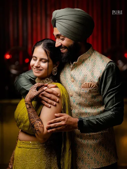 A sweet, candid moment from a Mehndi ceremony. The couple's embrace and happy expressions show their love and excitement.