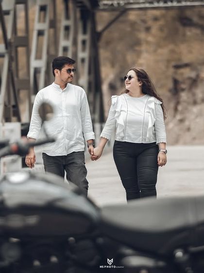A creative angle using the motorcycle to frame the couple as they walk hand-in-hand on the bridge. This adds depth and a unique perspective to the shot.