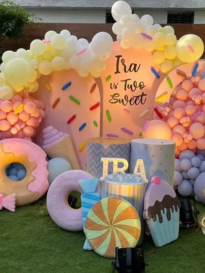A fun and colorful 'Two Sweet' candy-themed birthday party. This outdoor setup is filled with giant donut, ice cream, and candy props, along with pastel balloon arrangements, perfect for a second birthday.