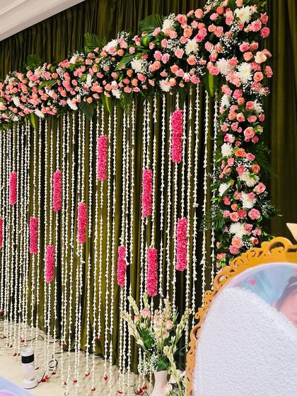 An elegant naming ceremony backdrop with hanging strings of jasmine and pink floral accents. The dark green curtain provides a rich contrast, making the flowers pop.