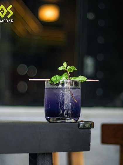 Dive into a world of flavors with our eclectic cocktail menu. This purple drink with a mint garnish is a perfect example.