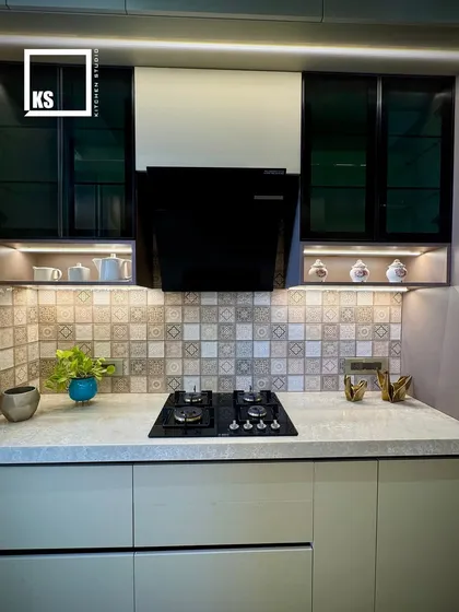 The combination of patterned tiles, black-framed glass cabinets, and a sleek chimney creates a balanced and visually interesting cooking area.